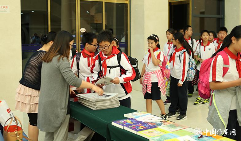 參加頒獎典禮的學(xué)生排隊入場，工作人員為他們分發(fā)當(dāng)天的《文藝報》兒獎特刊